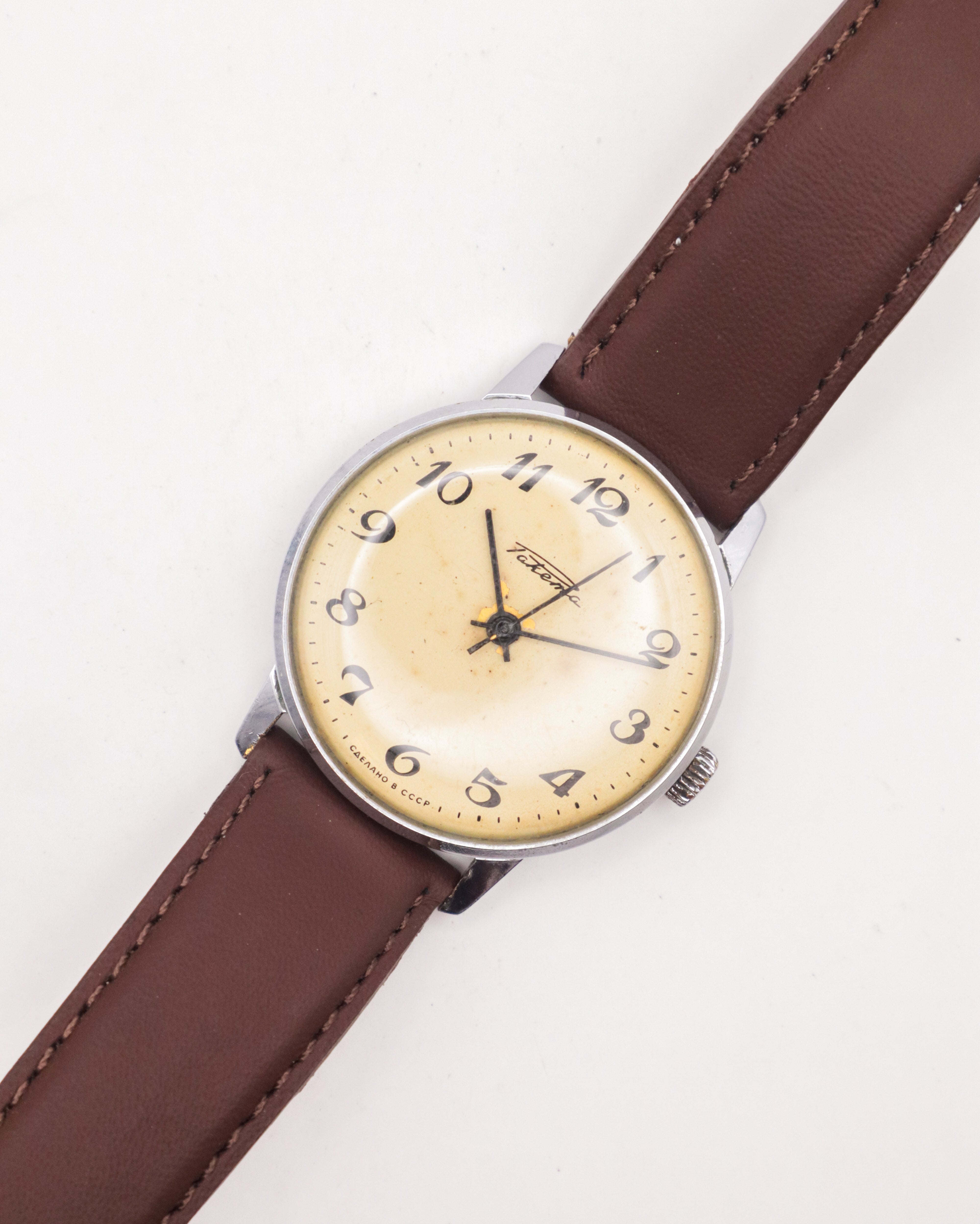 A silver Raketa 2609 watch with a white dial and brown leather strap.